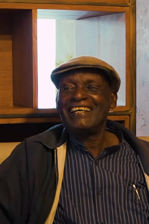 Mzee Daniel, Paints by Daniel, smiling in his flat cap