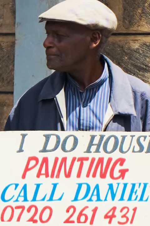 Mzee Daniel holding his hand-painted banner: I do house painting, call Daniel 0720 261 431